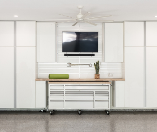 White garage cabinet system with a floating tall locker system, block work surface, and a mobile tool chest on wheels.