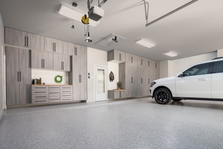 Garage with light gray flooring, greige cabinets, white walls and a white door.