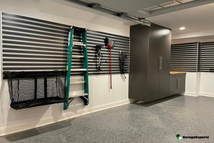 Garage with white walls, black and gray slatwall panels, and brown storage cabinets.